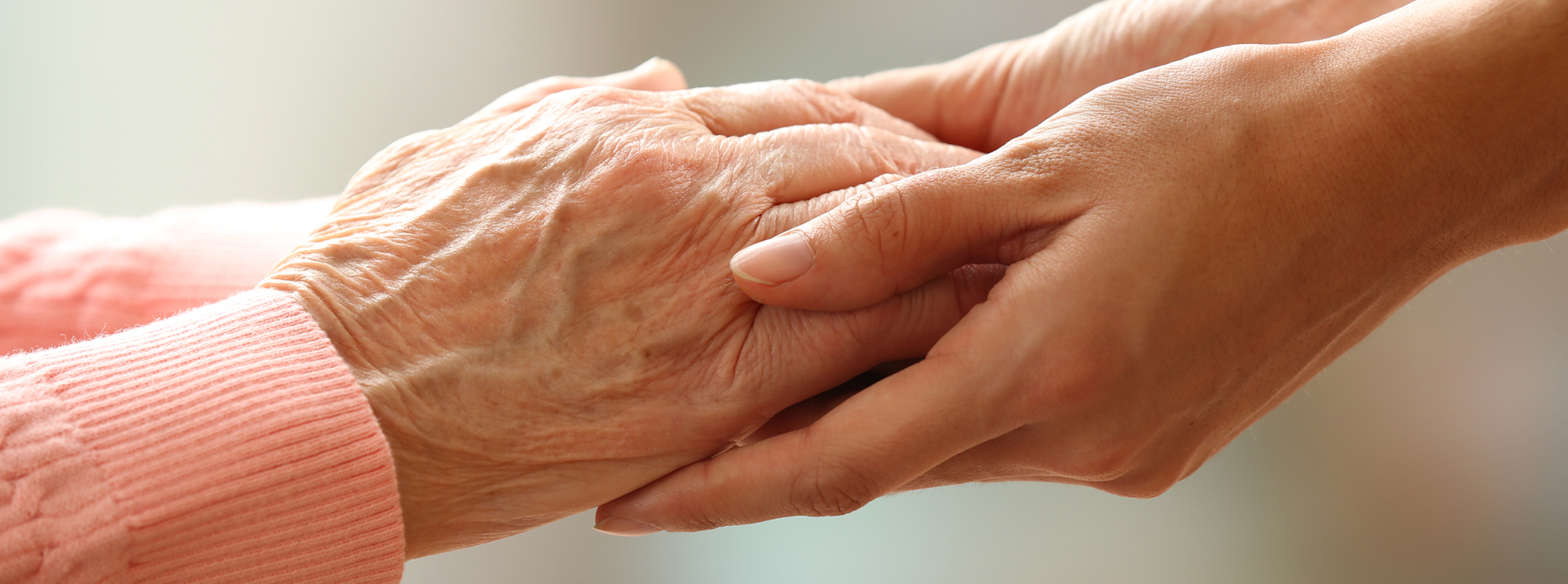 Old and young holding hands on light background, closeup